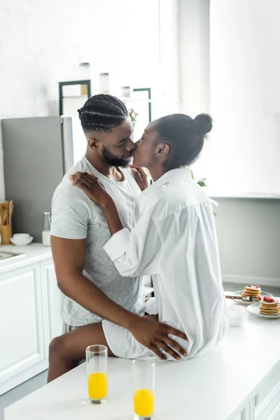 Passionate african american couple kissing on kitchen counter at kitchen — Stock Photo