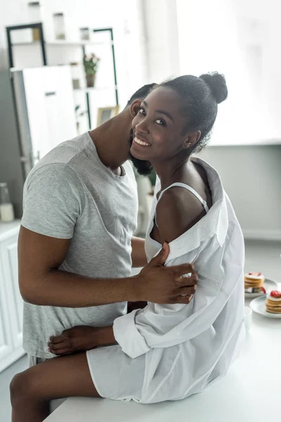 Afroamericano novio desvestirse y besar novia en cocina - foto de stock