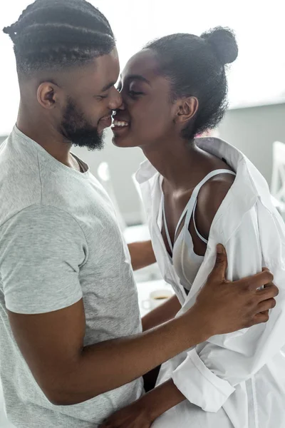 Vista laterale di sorridente africano americano fidanzato baciare fidanzata in cucina — Foto stock