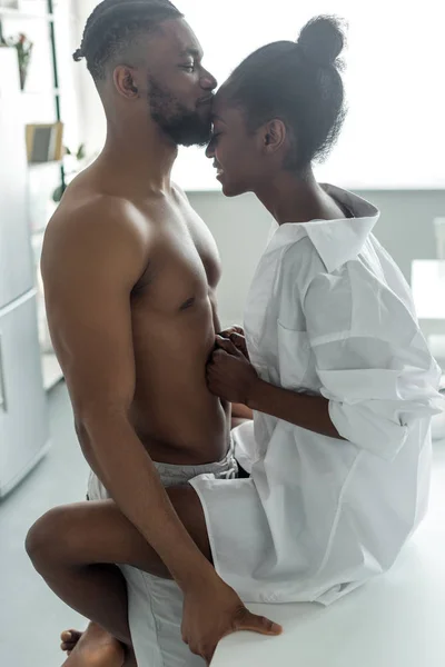 Vue latérale de sexy couple afro-américain embrasser sur le comptoir de la cuisine à la cuisine — Photo de stock