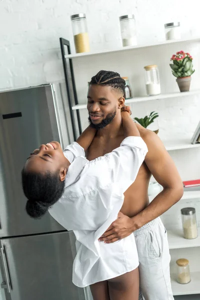 Africano americano pareja sonriendo y abrazando en cocina - foto de stock