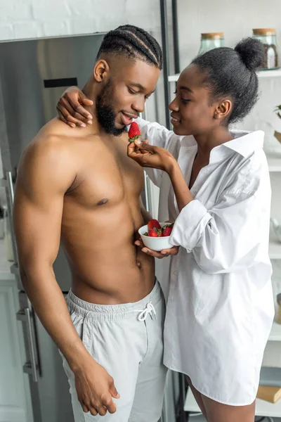 Africano americano novia alimentación novio con fresa en cocina - foto de stock