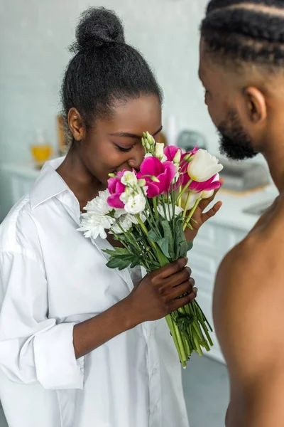African american girlfriend sniffing flowers at kitchen — Stock Photo