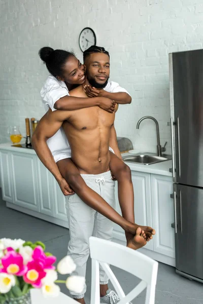Africano americano novio dando piggy nuevo a novia en cocina - foto de stock