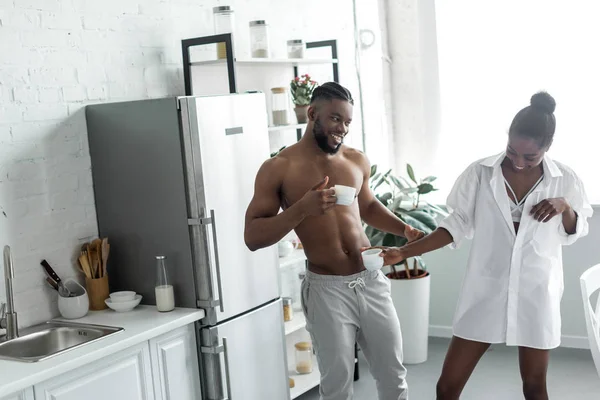 African american couple having fun with cups of coffee at kitchen — Stock Photo