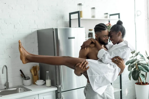 Africano americano novio holding novia en cocina - foto de stock
