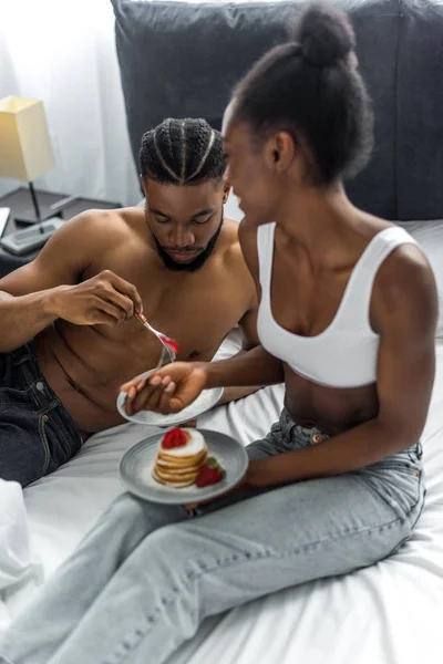 Africano casal americano comer deliciosas panquecas na cama no quarto — Fotografia de Stock