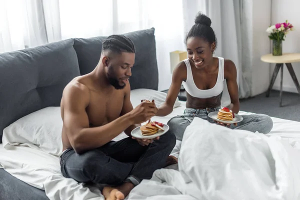 Pareja afroamericana comiendo panqueques en el dormitorio - foto de stock