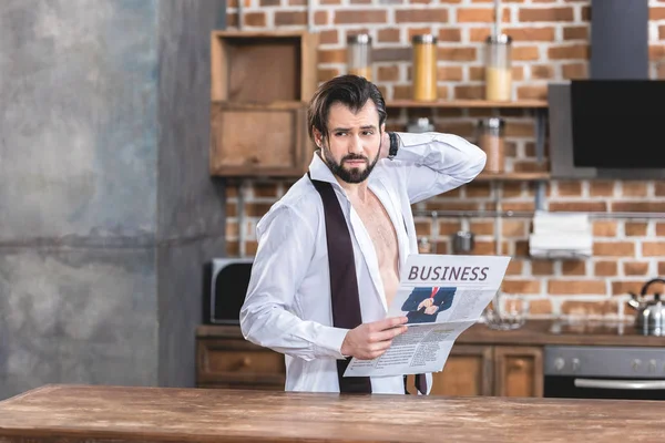 Раздраженный красивый одинокий бизнесмен держит газету и смотрит в сторону кухни — стоковое фото