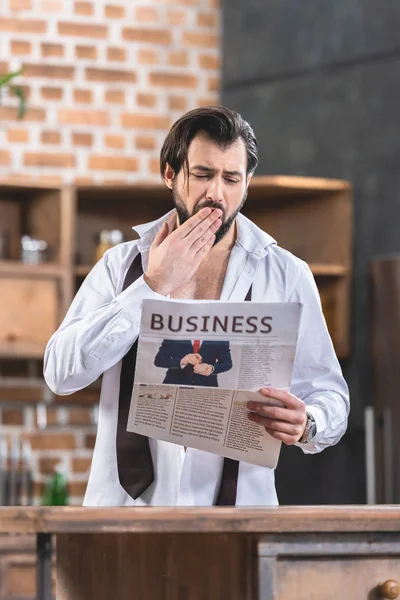 Guapo solitario hombre de negocios leyendo periódico y bostezando en la cocina - foto de stock