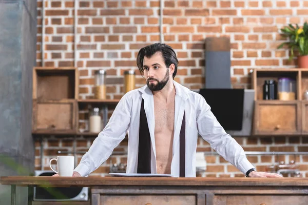 Belo solitário empresário de pé em camisa desabotoada na cozinha — Fotografia de Stock