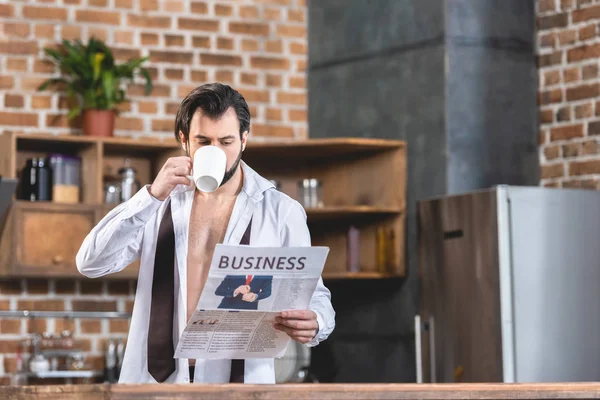 Bell'uomo d'affari solitario che beve caffè e legge giornali in cucina — Foto stock