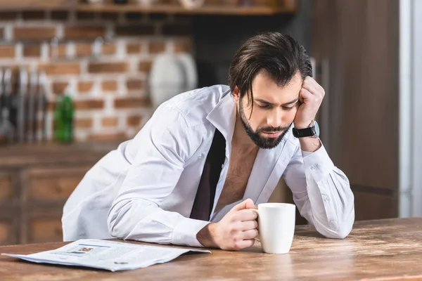 Stanco uomo d'affari solitario bello appoggiato sul tavolo con una tazza di caffè in cucina — Foto stock