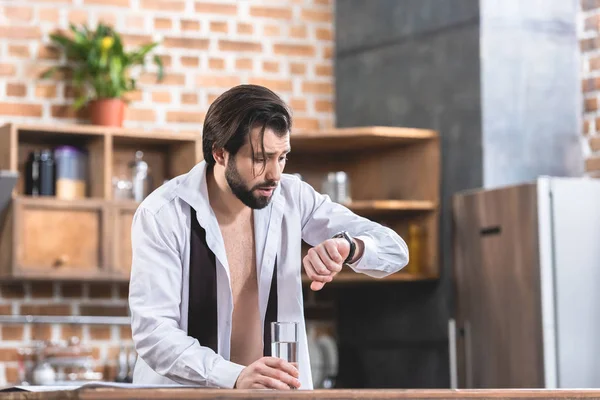 Handsome loner businessman with hangover checking time at kitchen — Stock Photo