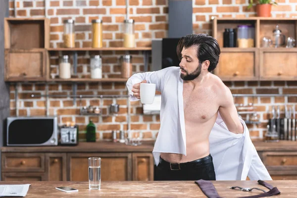 Bell'uomo d'affari solitario che indossa la camicia e tiene in mano una tazza di caffè in cucina — Foto stock