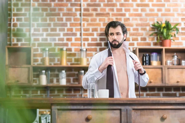 Handsome loner businessman with unbuttoned shirt looking away at kitchen — Stock Photo