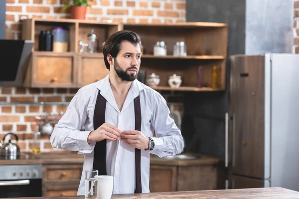Guapo solitario hombre de negocios abotonamiento camisa en la cocina - foto de stock