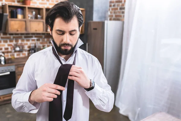 Handsome loner businessman tying necktie at home — Stock Photo