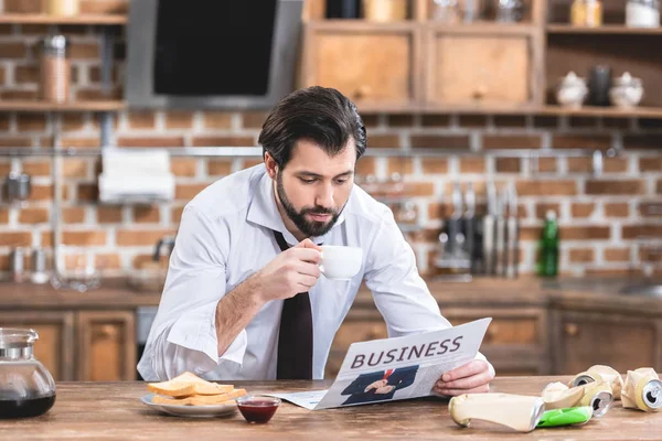 Bell'uomo d'affari solitario che beve caffè e legge giornali al mattino in cucina — Foto stock