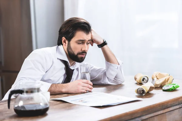 Beau homme d'affaires solitaire avec gueule de bois regardant des boîtes froissées sur la table à la cuisine — Photo de stock