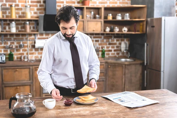 Uomo d'affari solitario allegro che aggiunge la marmellata su pane tostato a cucina — Foto stock