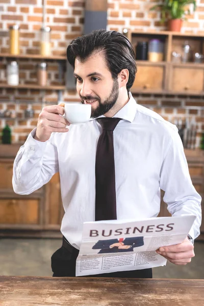 Bonito solitário empresário beber café e segurando jornal na cozinha — Fotografia de Stock