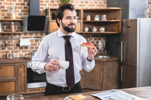 Guapo solitario hombre de negocios desayunando en la cocina - foto de stock