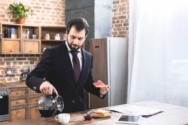 Schöner Einzelgänger Geschäftsmann schenkt Kaffee ein und hält Toast in der Küche — Stockfoto