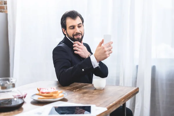 Sonriente hombre de negocios solitario tomando selfie con teléfono inteligente en la cocina - foto de stock