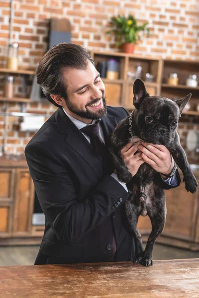 Sonriente solitario hombre de negocios sosteniendo perro en cocina - foto de stock