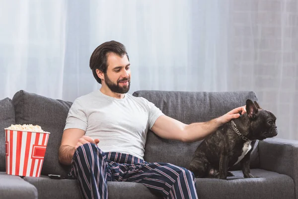 Handsome loner palming bulldog on sofa at home — Stock Photo