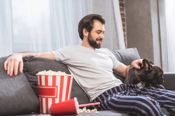 Lächelnder Einzelgänger palmt Bulldogge auf Sofa im Wohnzimmer — Stockfoto