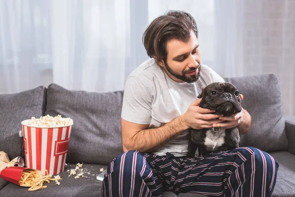 Schöner Einzelgänger umarmt Bulldogge auf Sofa im Wohnzimmer — Stockfoto