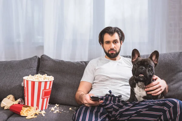 Guapo solitario viendo tv con bulldog en sofá en sala de estar - foto de stock