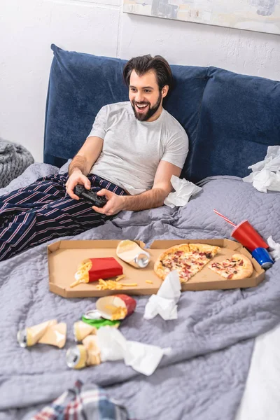 Sorridente solitario maschio che gioca al videogioco in camera da letto — Foto stock
