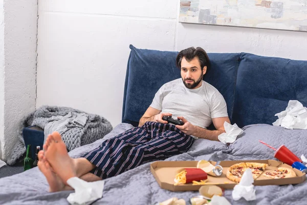 Hombre solitario jugando videojuego en la cama en el dormitorio - foto de stock