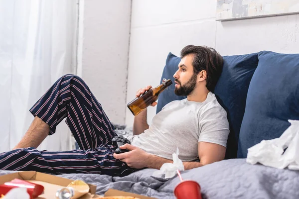 Macho solitario jugando videojuego en el dormitorio y bebiendo cerveza - foto de stock