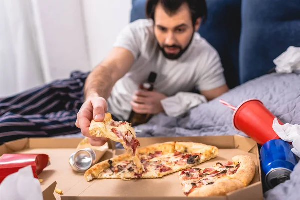 Schöner Einzelgänger, der ein Stück Pizza auf dem Bett im Schlafzimmer nimmt — Stockfoto