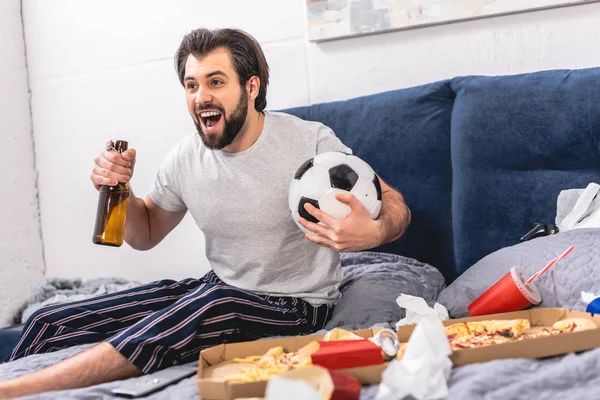 Handsome loner watching football game with beer and screaming in bedroom — Stock Photo