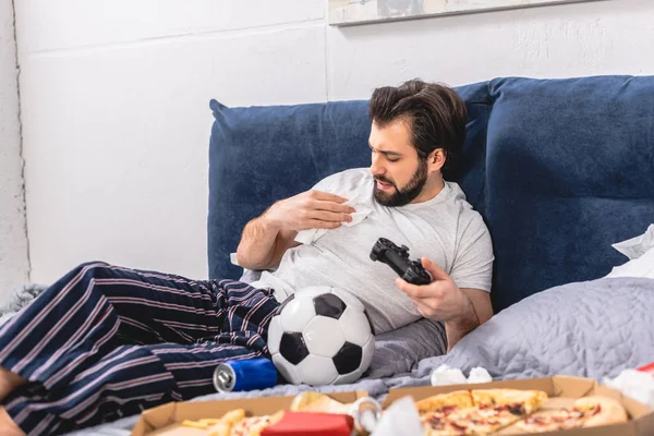 Male loner playing video game in bedroom and removing spot on shirt — Stock Photo