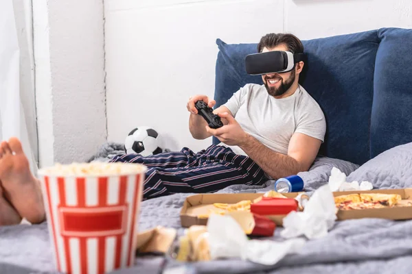 Sorridente solitario utilizzando cuffie realtà virtuale e giocare al videogioco in camera da letto — Foto stock