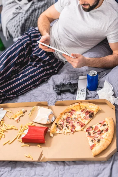 Imagem cortada de solitário usando tablet com pizza na cama no quarto — Fotografia de Stock