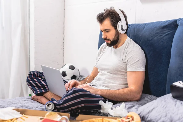 Guapo solitario escuchar música y el uso de ordenador portátil en el dormitorio - foto de stock