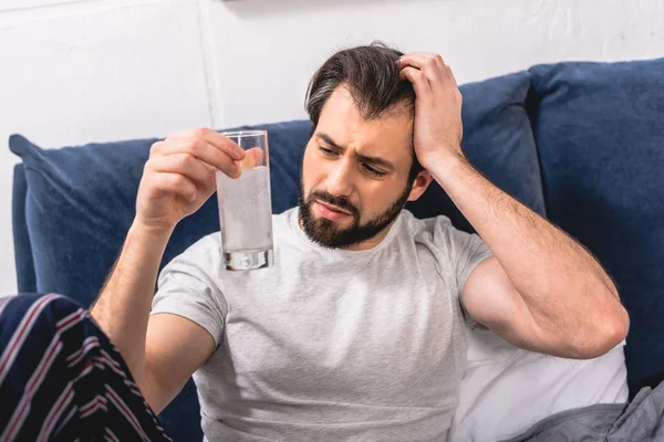 Loner having headache with hangover and looking at glass with pill and water in bedroom — Stock Photo