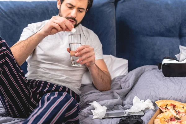 Loner having headache with hangover and putting pill into glass of water in bedroom — Stock Photo