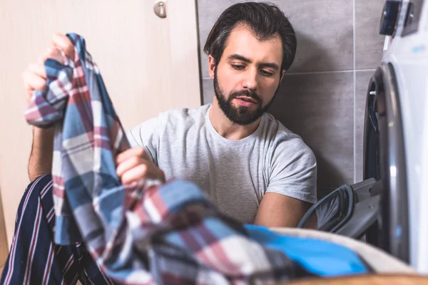 Guapo solitario tomando ropa para lavar cerca de la lavadora en el baño - foto de stock