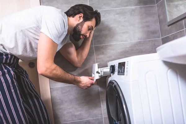 Seitenansicht eines gutaussehenden Einzelgängers mit Blick auf die Waschmaschine im Badezimmer — Stockfoto