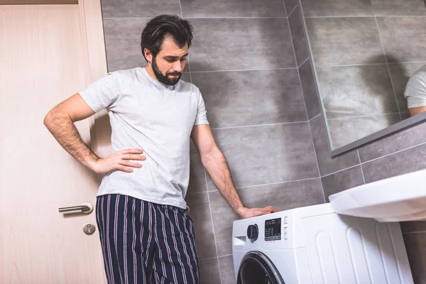 Schöner Einzelgänger lehnt an Waschmaschine im Badezimmer — Stockfoto