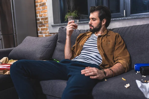 Solitario mirando un vaso de whisky en la sala de estar - foto de stock