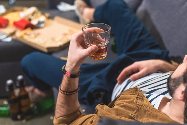 Обрезанный одиночка лежит на диване со стаканом виски в гостиной — стоковое фото